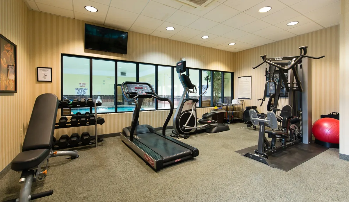 A well-equipped fitness center with treadmills, ellipticals, a weight bench, and a dumbbell rack, designed for individual workouts or group exercise. The space is bright and motivating, with ample equipment for guests to stay energized.
