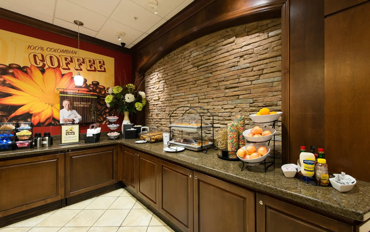A cozy coffee station is set alongside a variety of snacks and fresh fruits. Decorative wall art and comfortable touches invite guests to enjoy a relaxed atmosphere, perfect for a quick breakfast, morning coffee, or light snack.