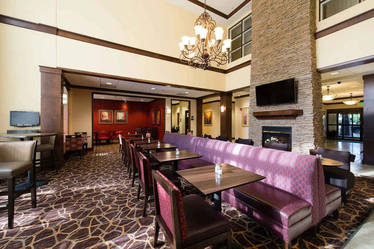 A welcoming communal lounge featuring a chandelier and a cozy fireplace, surrounded by comfortable seating areas. Guests can be seen engaging in relaxed conversations and casual dining, emphasizing a lively social atmosphere. The space exudes warmth and encourages both quiet moments and group gatherings.