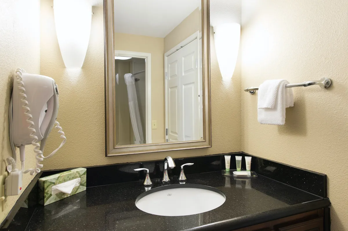 A bright, modern bathroom with a well-lit mirror above the sink, neatly arranged fresh towels, complimentary toiletries on the counter, and soft lighting fixtures, all contributing to a sense of comfort and cleanliness.