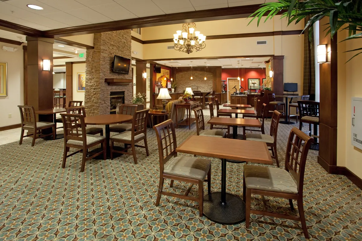 A welcoming room filled with tables and chairs, accented by a fireplace, decorative plants, and a chandelier, creates a flexible environment for both casual dining and relaxing with friends. The space is suitable for community events, game nights, or themed dinners, capturing the essence of group fun and downtime.