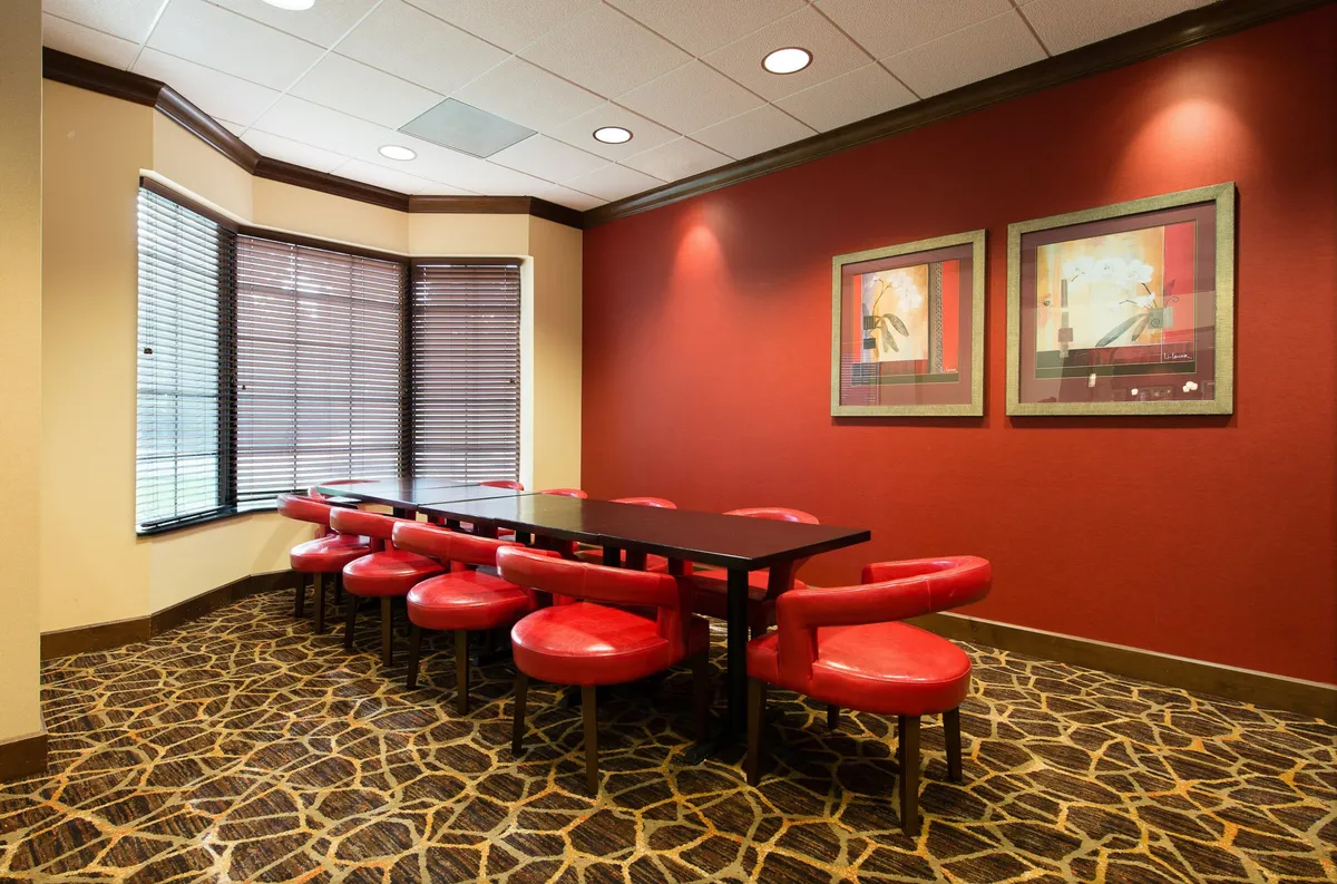 A contemporary dining area featuring a long black table with striking red chairs and modern artwork on the wall. The setting is suited for both shared meals and remote work, reflecting the multi-purpose use of the dining space.