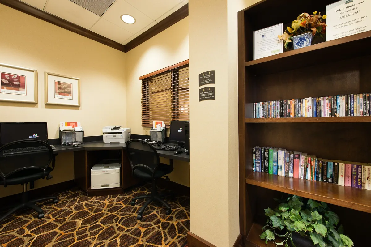 A quiet, inviting business center with computers, a printer, bookshelves, and framed art, ideal for guests needing a dedicated work area or a spot to read and brainstorm.