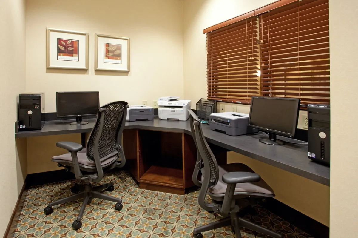The business center is equipped with desks, computers, printers, and framed artwork, providing an organized environment for productive work. The layout and resources support remote work and essential business tasks.