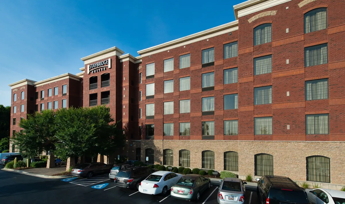 This image captures the hotel's brick facade with large windows, a welcoming entry, and a landscaped area set against the parking lot. The inviting architecture and lush greenery create a sense of arrival and anticipation, ideal for families setting out for local adventures.